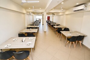 A long dining hall with multiple tables and chairs, ceiling fans, and an air conditioning unit. -  Hotel Akshar Imperial Morbi (Morbi)