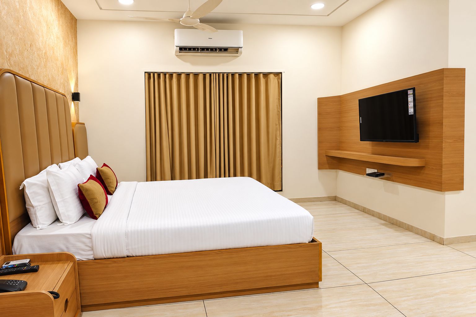 Una camera d'albergo con un letto, una TV a muro, un condizionatore d'aria e una tenda.