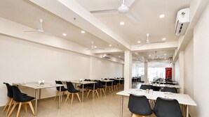 A spacious conference room with multiple tables and chairs, ceiling fans, and an air conditioning unit. -  Hotel Akshar Imperial Morbi (Morbi)