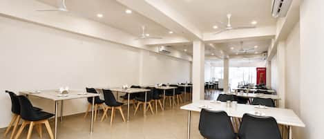 A spacious conference room with multiple tables and chairs, ceiling fans, and an air conditioning unit.