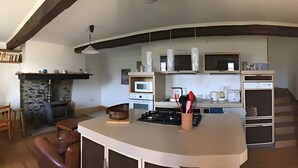 A modern kitchen with a central island, built-in appliances, and a stone fireplace. - Maison de fontale, mountain retreat with breathtaking views (Aleu)
