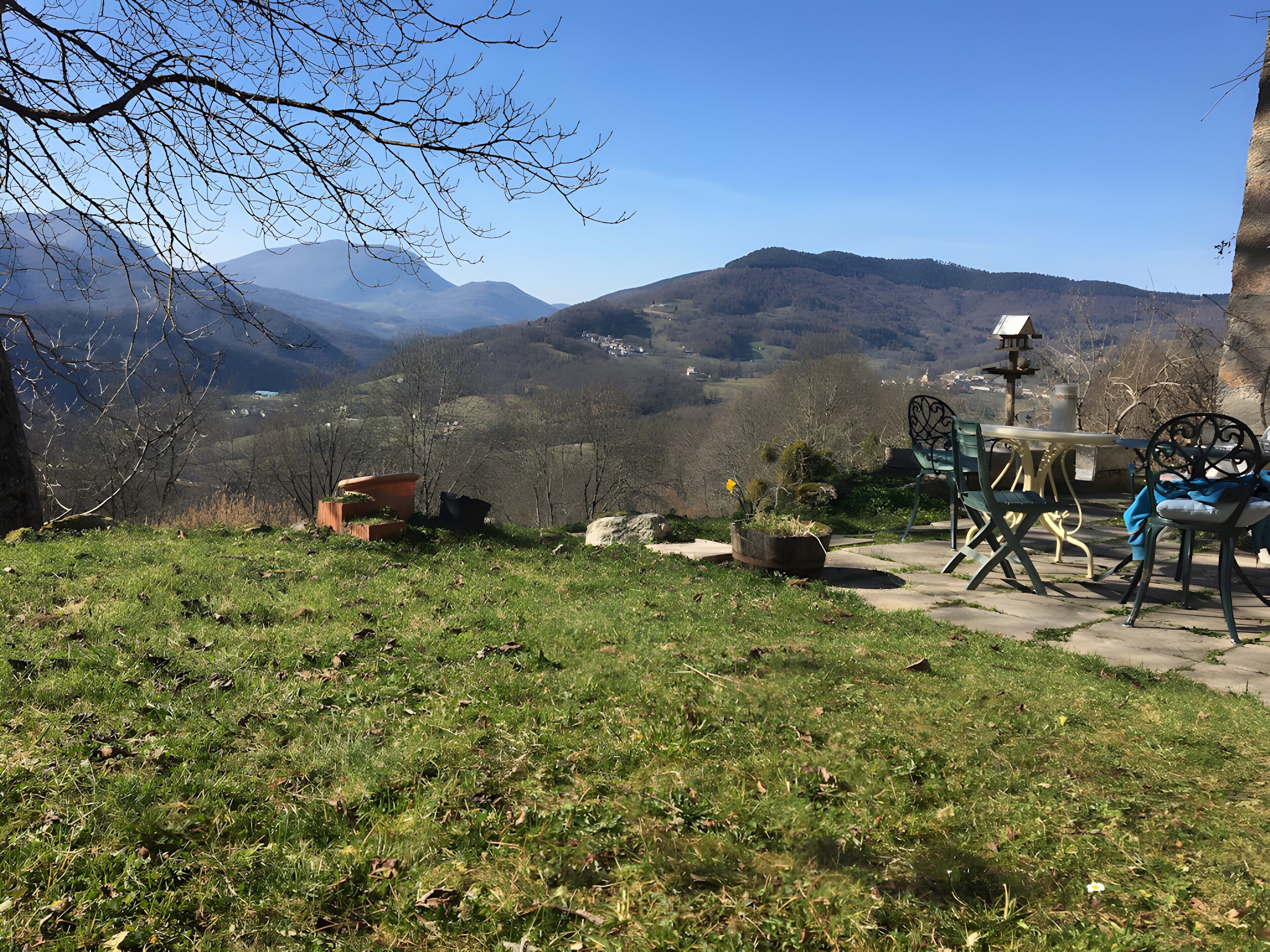 Eine Terrasse mit Gartenmöbeln, Blick auf Berge und einem gepflasterten Weg.