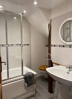 Ein Badezimmer mit Duschkabine aus Glas, Toilette, Waschbecken und Spiegel.