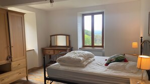 A bedroom with a bed, wooden wardrobe, dresser, dresser drawers, a nightstand, a lamp, a window, and a mirror. - Maison de fontale, mountain retreat with breathtaking views (Aleu)