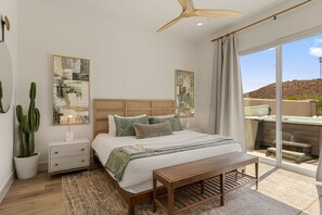 Un dormitorio con cama, mesitas de noche, ventilador de techo, obras de arte, un cactus en maceta y vistas al exterior.
