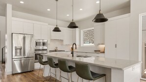A modern kitchen with a central island, stainless steel appliances, and bar stools. - Golf Course Views: Pool + Golf Course Views (Washington)