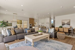 Ein modernes Wohnzimmer mit einem grauen Sofa, einem Holztisch und einem Essbereich mit Tisch und Stühlen.