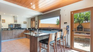 Une cuisine moderne dotée d’un grand îlot central, d’un plafond en bois et d’une porte-fenêtre coulissante donnant sur un espace extérieur.