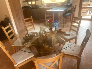 Une table ronde en verre, entourée de chaises en bois, une cuisine en arrière-plan et un coin repas avec des chaises et une table.