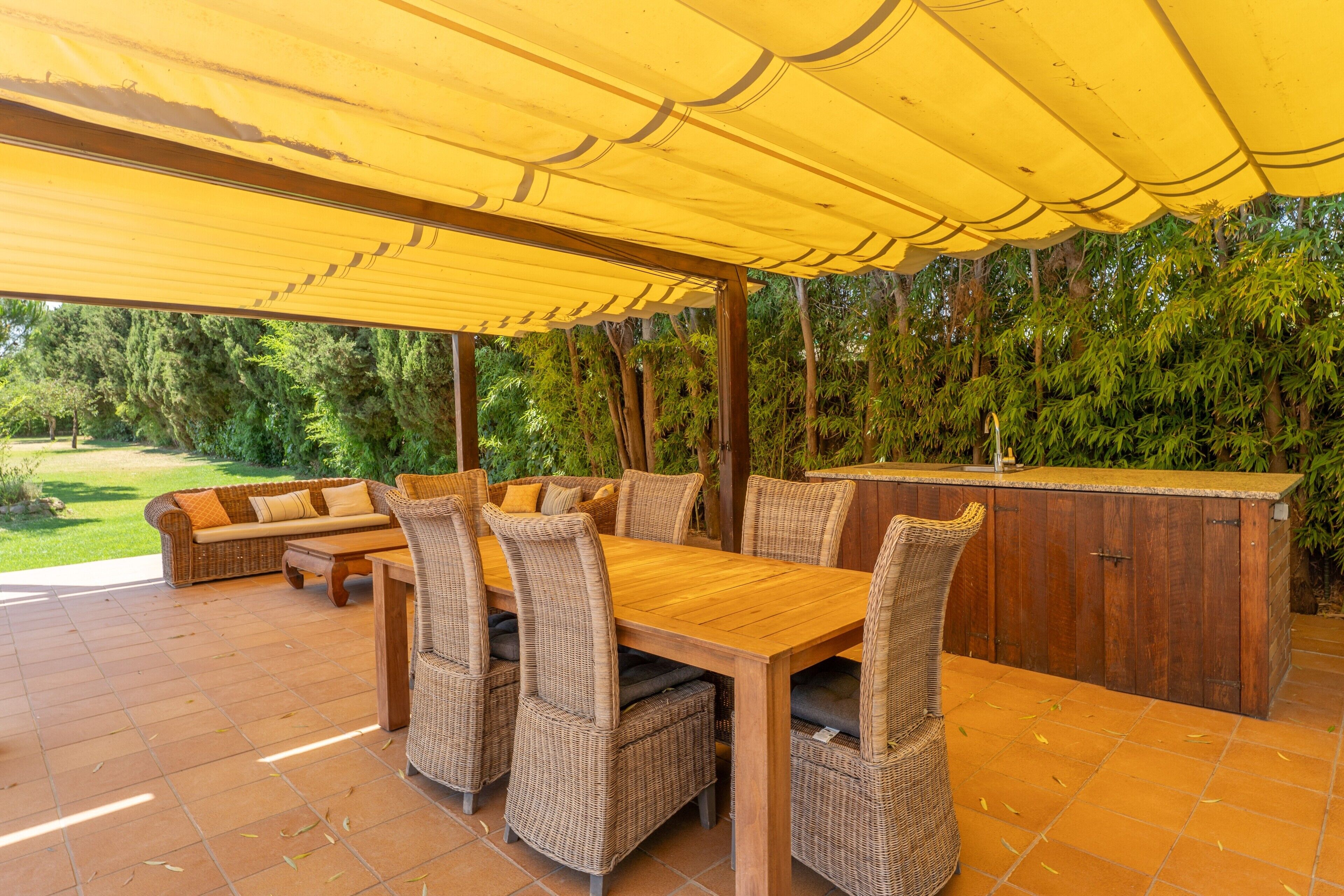 An outdoor dining area with a wooden table and wicker chairs, a bar counter, and a covered patio.