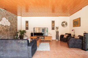 A living room with a stone wall, wooden ceiling, a flat-screen TV, two sofas, a coffee table, and a speaker. - Villa in Llofriu with Pool (Palafrugell)
