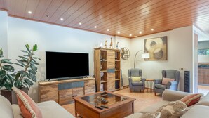 Un salon comprenant un téléviseur, un meuble de rangement en bois, un canapé et une table basse en verre.