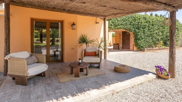 Un patio couvert aménagé avec un canapé en osier, une petite table ronde et une plante en pot.