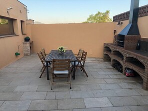 Une terrasse extérieure avec une table et des chaises, un four en briques et une caméra de surveillance fixée au mur.