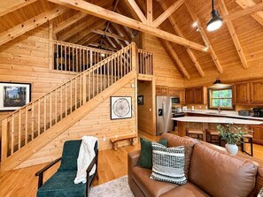 A wooden cabin interior with a staircase, living room, kitchen, and a dining area. - 2BR w/Hot Tub*Fire Pit*Games*Privacy*Walk to Pool! (Sevierville)