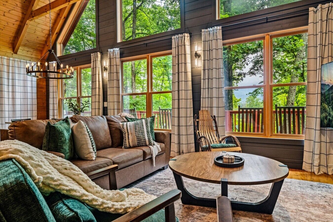 A cozy living room with a leather sofa, a round coffee table, and large windows with curtains.