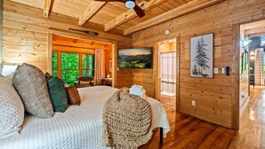 A wooden cabin bedroom with a bed, pillows, a blanket, a painting, and a ceiling fan. - 2BR w/Hot Tub*Fire Pit*Games*Privacy*Walk to Pool! (Sevierville)