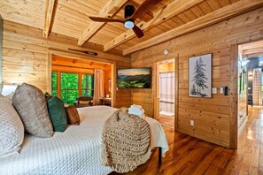 A wooden cabin bedroom with a bed, pillows, a blanket, a painting, and a ceiling fan. - 2BR w/Hot Tub*Fire Pit*Games*Privacy*Walk to Pool! (Sevierville)