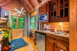 L’intérieur d’un chalet en bois comprend un coin cuisine, une table à manger et une grande fenêtre donnant sur un paysage verdoyant.