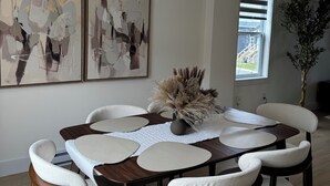 Un comedor con una mesa redonda, sillas blancas acolchadas, una obra de arte abstracta en la pared y una planta en maceta.