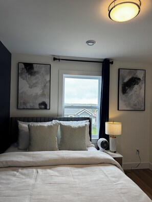 A bedroom with a bed, a window, a ceiling light, and two abstract paintings on the walls. - New Luxury 3-Bedroom Getaway| Parking| Patio (St. John's)
