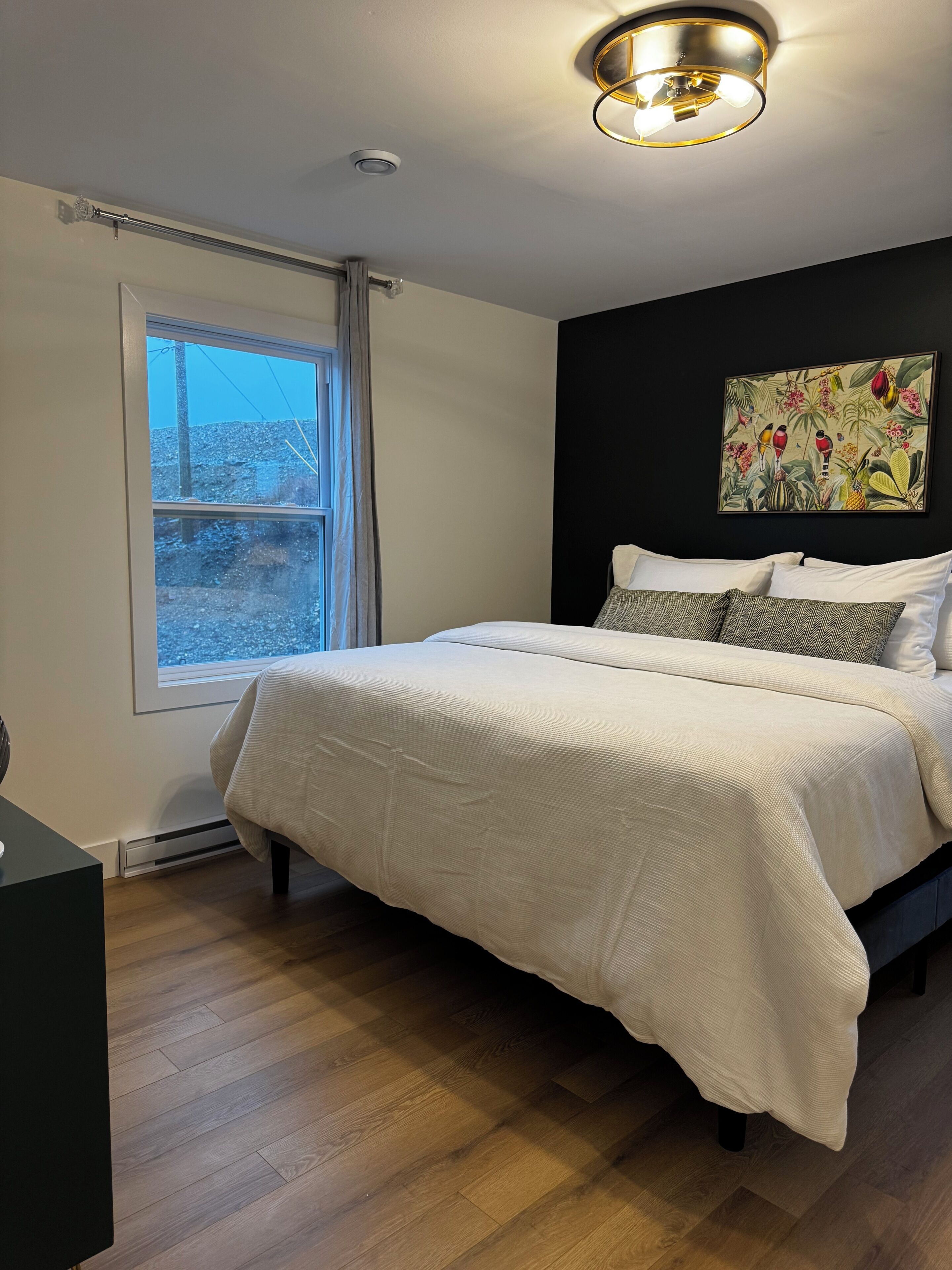 A bedroom with a bed, a window, a ceiling light, and a wall-mounted painting.