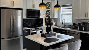 Una cocina moderna con una isla central, electrodomésticos de acero inoxidable, iluminación colgante y piso de mármol.