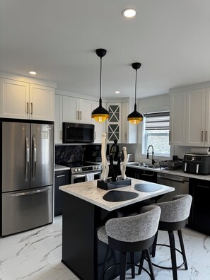A modern kitchen with a central island, stainless steel appliances, pendant lighting, and a marble floor. - New Luxury 3-Bedroom Getaway| Parking| Patio (St. John's)