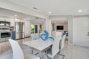 A modern kitchen with stainless steel appliances, a white dining table with chairs, and a decorative blue sculpture.