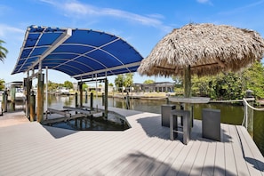 A wooden dock with a thatched-roof structure, a blue canopy, and a small pool.