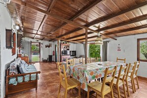 A dining area with a wooden table and chairs, a sofa with cushions, and a ceiling with wooden beams.