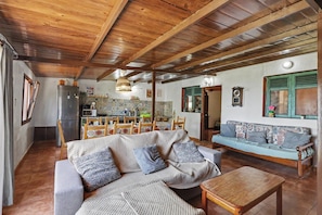 A cozy living room with a wooden ceiling, a sofa, a coffee table, and a dining area with chairs and a table.