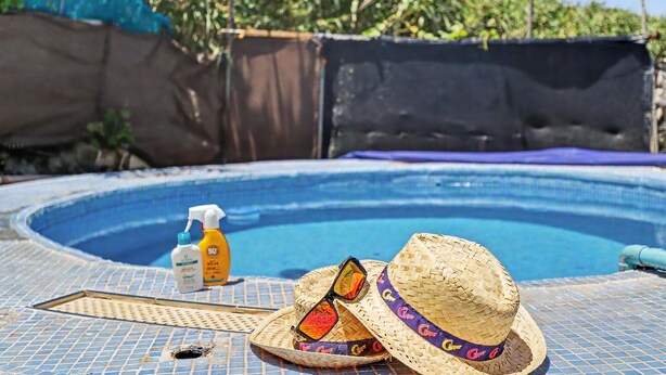A swimming pool with a tiled deck, a sun hat, sunglasses, and sunscreen bottles. - Finca El Lomo with Mountain Views, Private Pool and Wi-Fi (Saucillo)