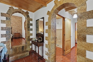 A room with stone arches, a wooden ceiling, a mirror, a wooden dresser, and a tiled floor.