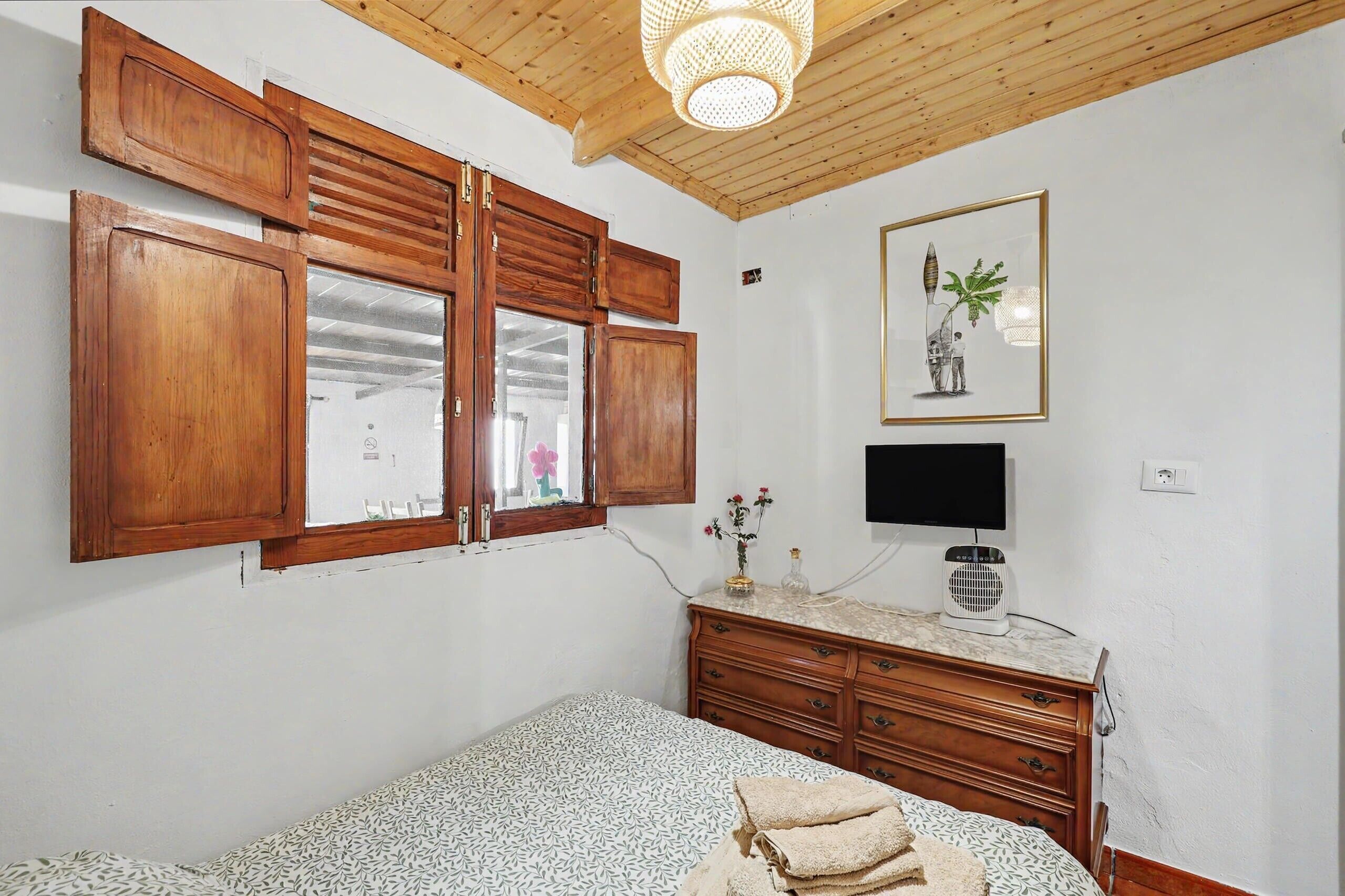 Un dormitorio con armarios de madera, una cama con ropa de cama estampada, un televisor y un ventilador de techo.
