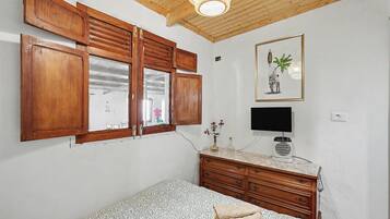 Un dormitorio con armarios de madera, una cama con ropa de cama estampada, un televisor y un ventilador de techo.