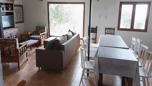A living room with a sofa, a TV, a dining table with chairs, and a window with a view of trees. - Finca El Lomo with Mountain Views, Private Pool and Wi-Fi (Saucillo)