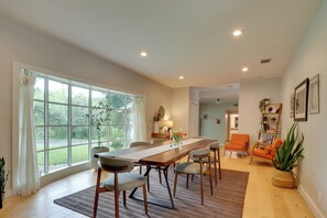 A spacious dining area with a long table, chairs, and a view through large windows.