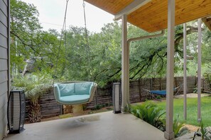 A covered patio with a hanging swing, a hammock, and a tall planter.