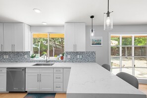 A modern kitchen with white cabinets, a marble countertop, and a large window.