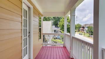 A wooden porch with a red floor, white railings, and a view of a residential street.