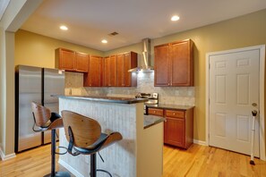 A kitchen with wooden cabinets, a stainless steel refrigerator, a built-in island with bar stools, and a white door.