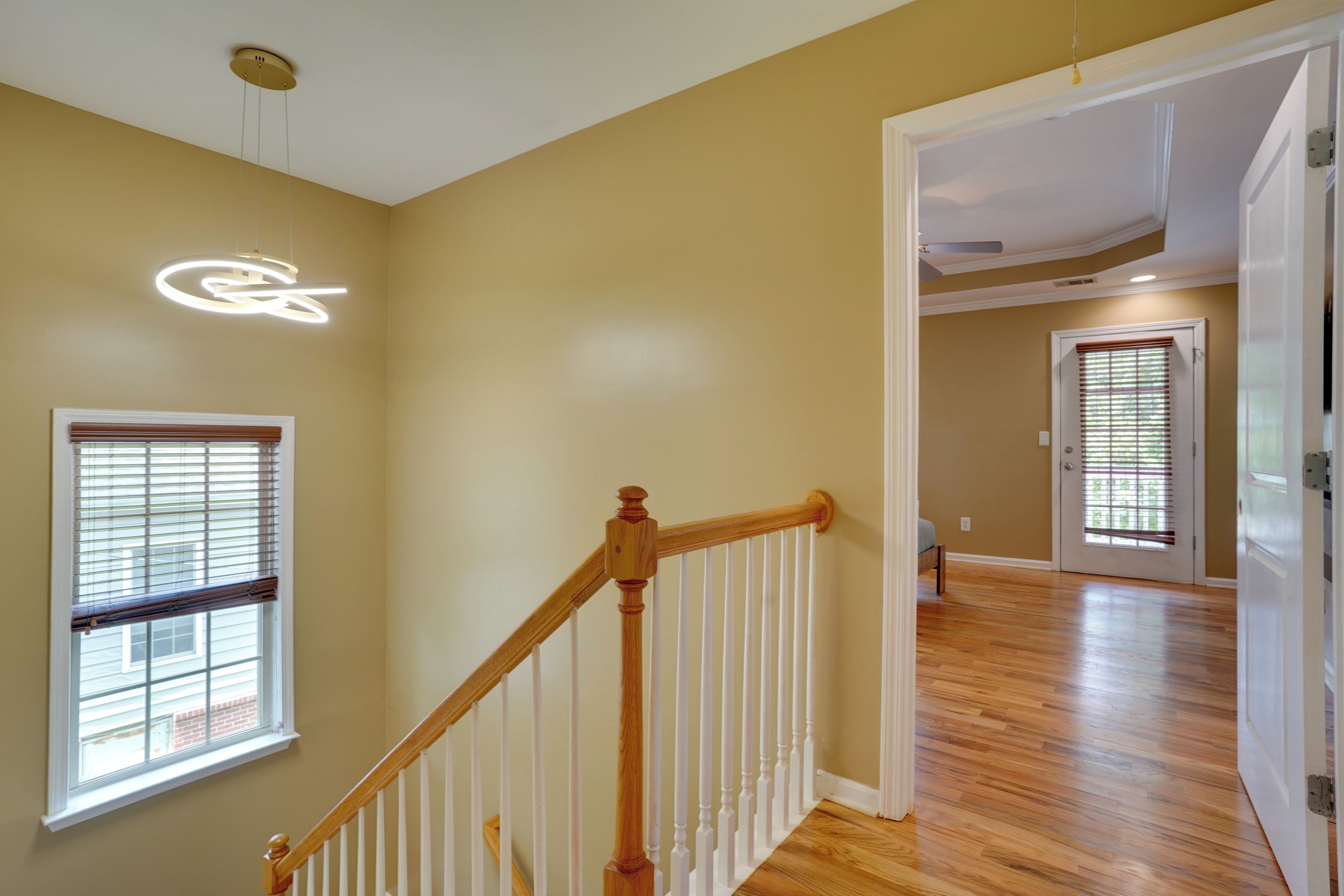 A spacious room with wooden flooring, a staircase with white railings, and a ceiling light fixture.