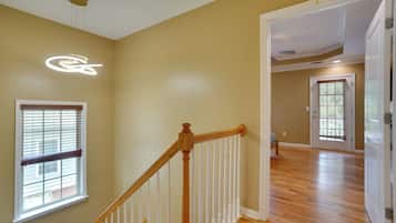 A spacious room with wooden flooring, a staircase with white railings, and a ceiling light fixture.