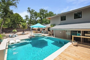A swimming pool with a wooden deck, lounge chairs, and a covered patio area.