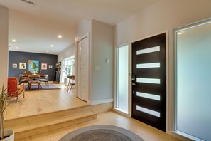 A modern interior with a staircase leading to a dining area, a black door with horizontal stripes, and a light-colored wall.