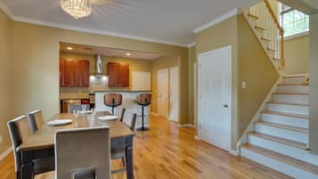 A spacious dining area with a wooden table and chairs, a kitchen with wooden cabinets and a chimney, and a staircase leading to another level.