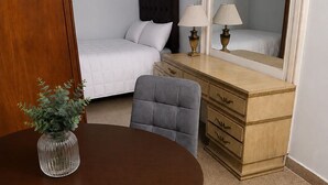 Ein Hotelzimmer mit einem Bett, einem Schminktisch, einem Spiegel, einem Tisch mit einer Vase und einem Stuhl.