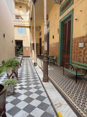A corridor with checkered flooring, columns, potted plants, and a bench. - Histórico (Buenos Aires)
