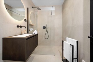 Une salle de bain moderne avec un grand miroir, un meuble-lavabo foncé, une douche équipée d’un pommeau de douche à main et un porte-serviettes.